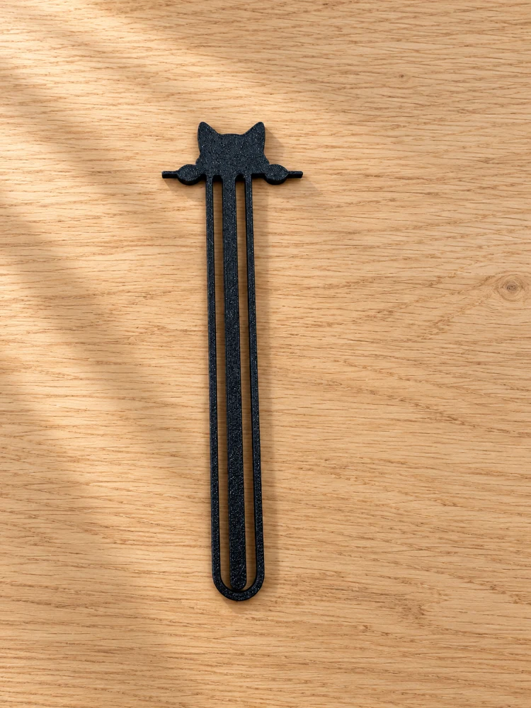 Black cat-shaped clip bookmark on a light oak tabletop