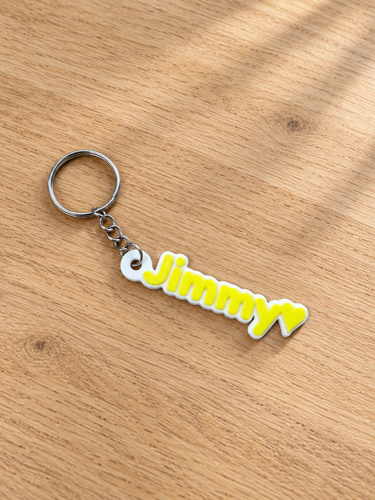 Jimmy keychain with yellow lettering and heart, white backing and a metal keyring on a light oak tabletop